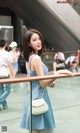 A woman in a blue dress standing next to a railing.