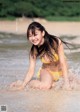 A woman in a yellow bikini sitting in the water.