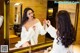 A woman in a white robe applying lipstick in front of a mirror.